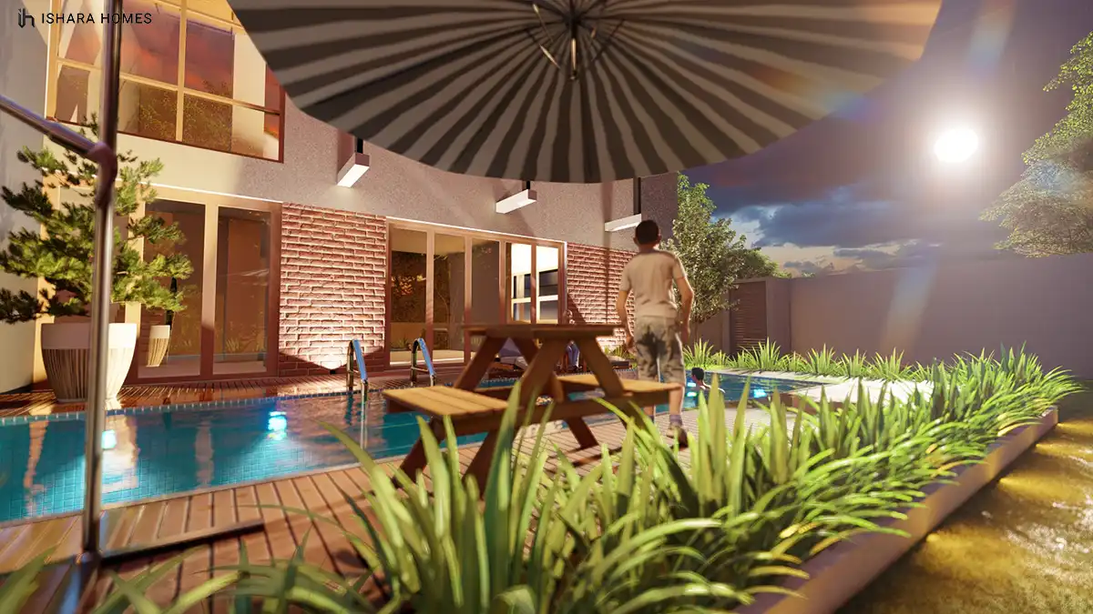 The same poolside scene after dark, the striped umbrella and warm wall lights glowing against the brick wall while the pool ripples under...